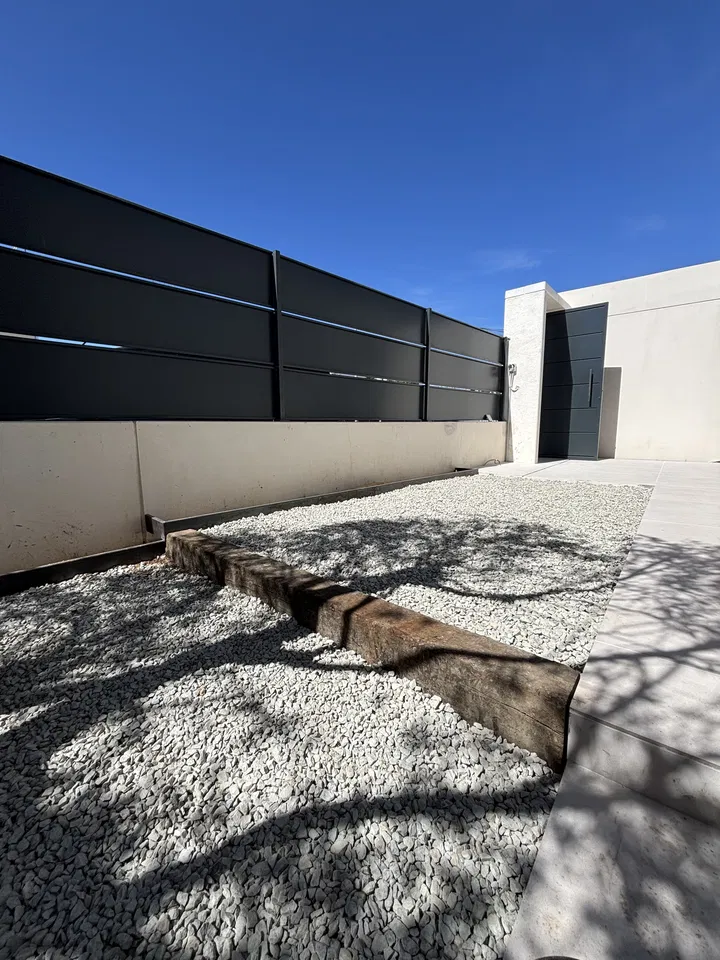 Zona exterior con grava clara, piezas de piedra y cerramiento oscuro; fotografía 1 de esta serie