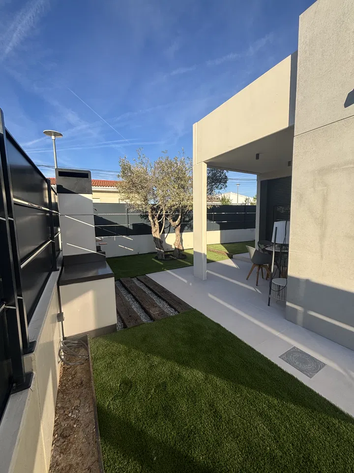 Jardín junto a una vivienda contemporánea, con césped y pavimento claro; fotografía 2 de esta serie