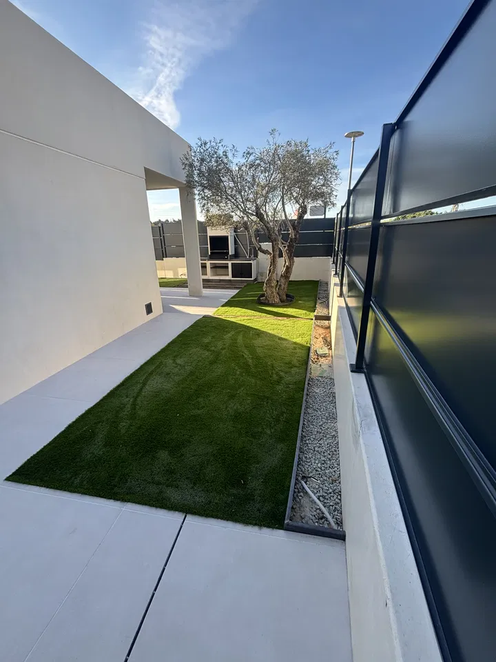 Jardín junto a una vivienda contemporánea, con césped y pavimento claro; fotografía 3 de esta serie